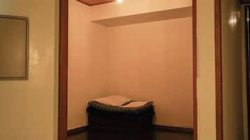 A small, dimly lit room with a single bed and a light fixture on the ceiling.