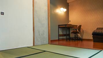 A room with tatami mats, a desk with a chair, and a wall-mounted light fixture.
