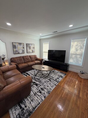 A modern living room with a brown leather sofa, a coffee table, and a flat-screen TV.