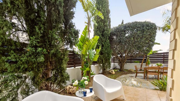 Een terras met twee witte stoelen, een klein rond tafeltje en een bloempot.