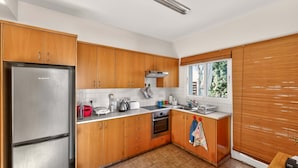 Een moderne keuken met houten kastjes, een roestvrijstalen koelkast, een gasfornuis en een raam met zonwering.