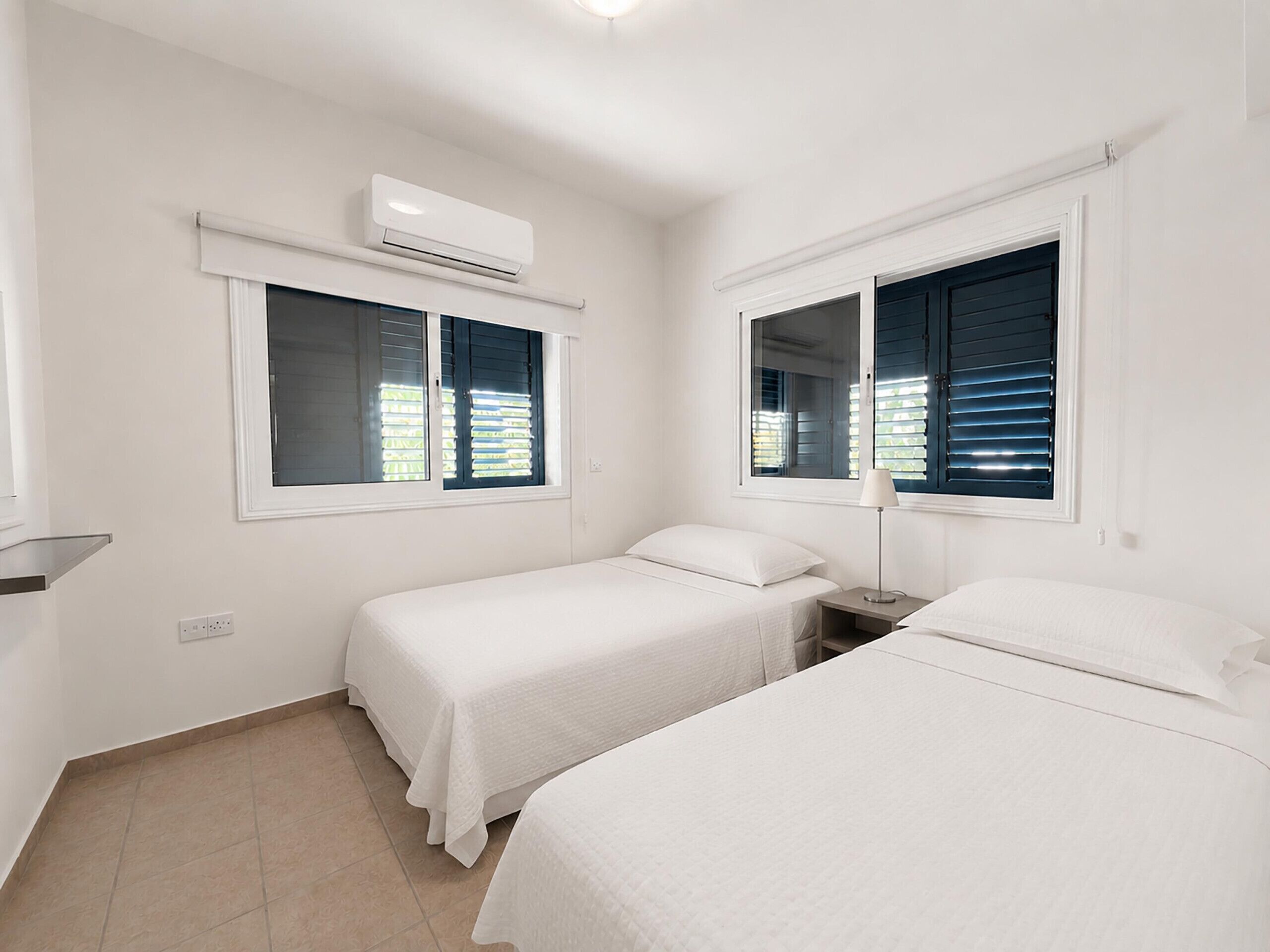A hotel room with two beds, an air conditioning unit, and windows with blinds.