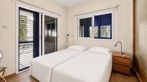 Een slaapkamer met twee bedden, een nachtkastje, een lamp en een schuifdeur naar een balkon.