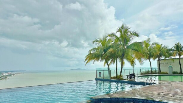 Une piscine à débordement offrant une vue sur l’océan et les palmiers.