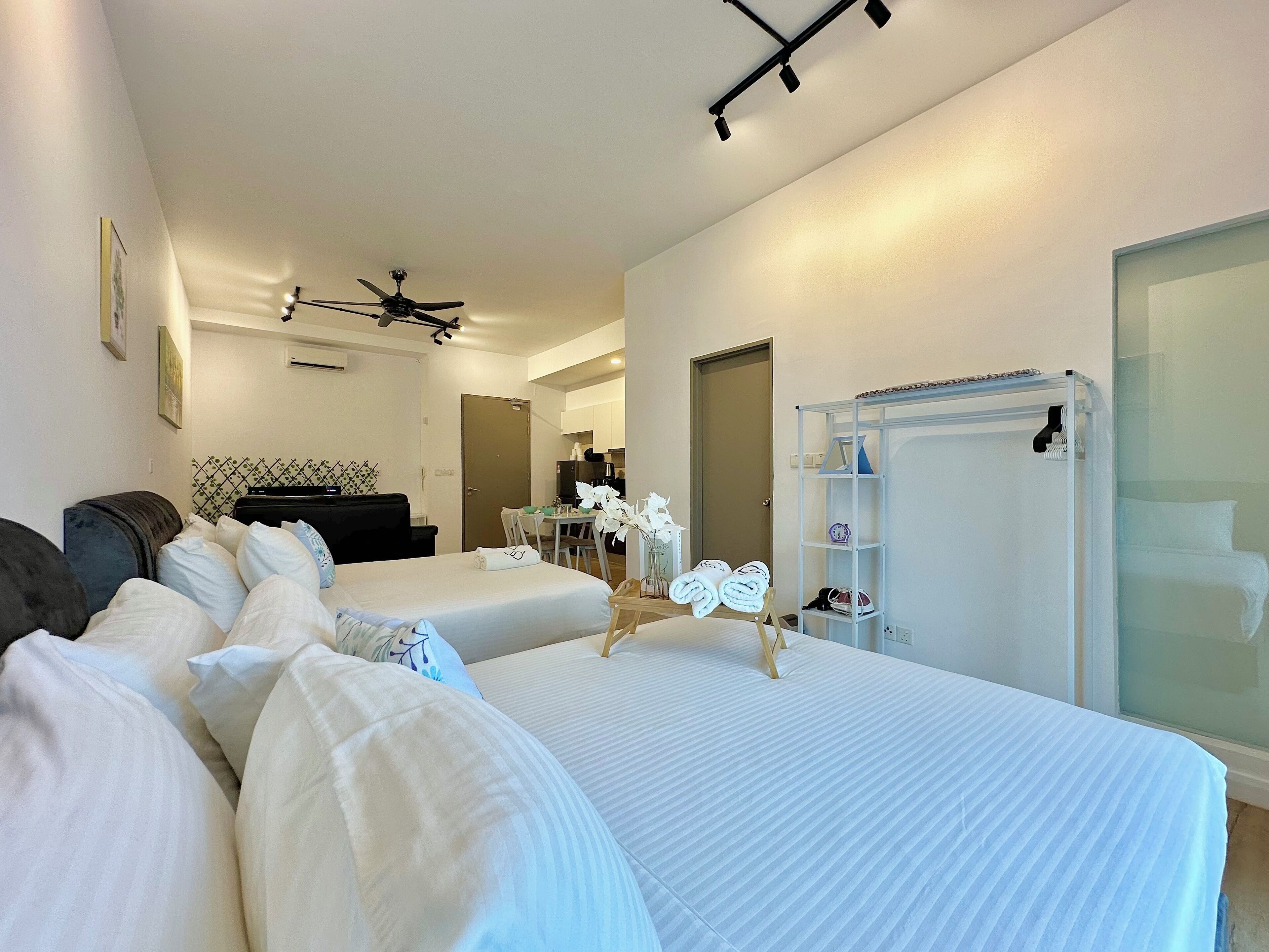 A hotel room with two beds, a ceiling fan, a small dining area, and a glass shower enclosure.
