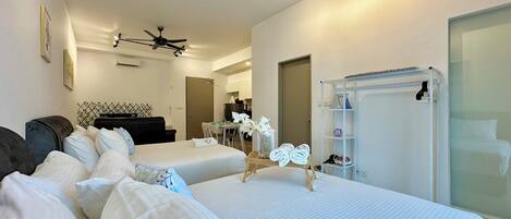 A hotel room with two beds, a ceiling fan, a small dining area, and a glass shower enclosure.