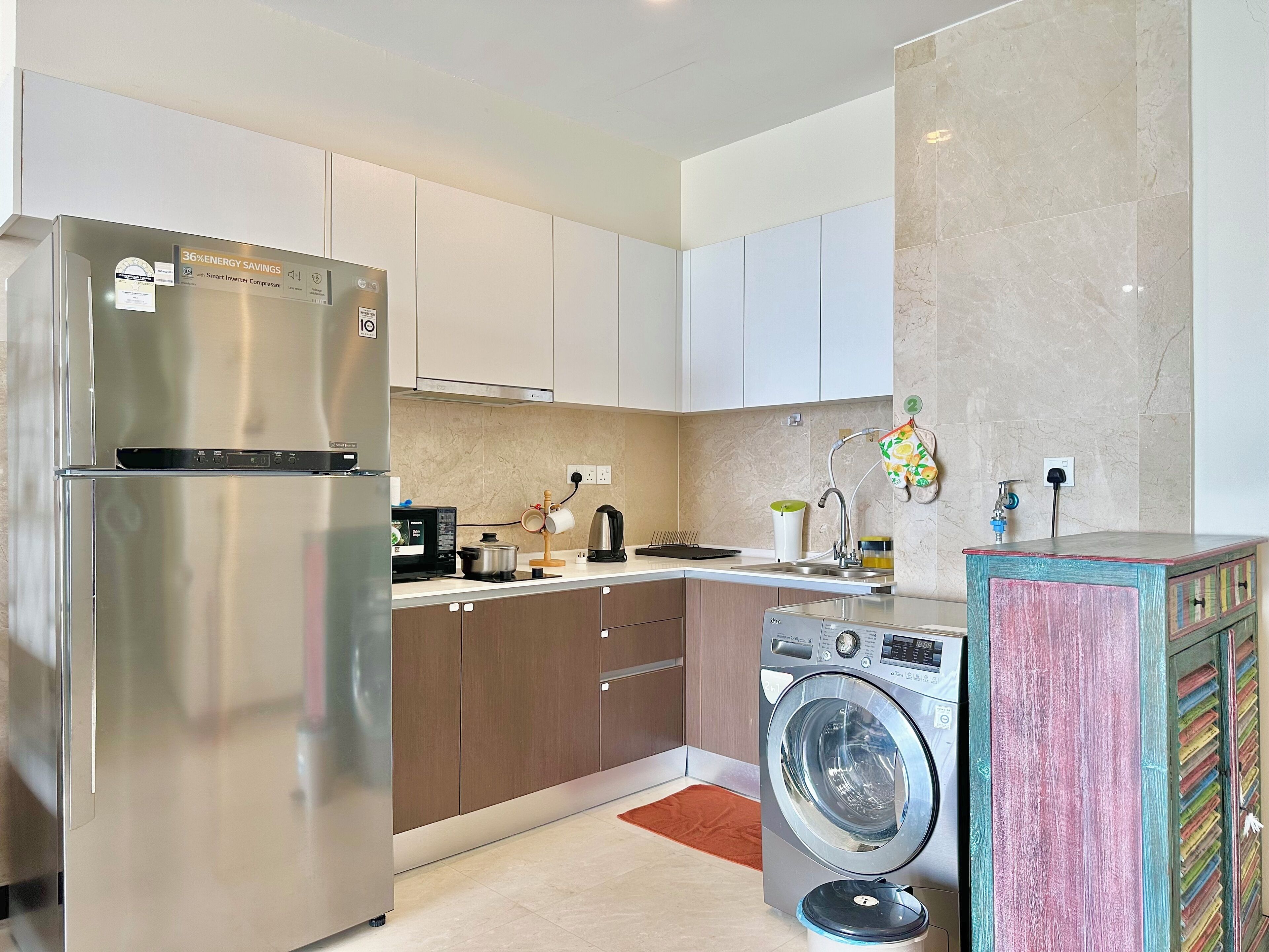 Une cuisine moderne dotée d’appareils électroménagers en acier inoxydable, d’un lave-linge encastré et d’une armoire aux couleurs vives.
