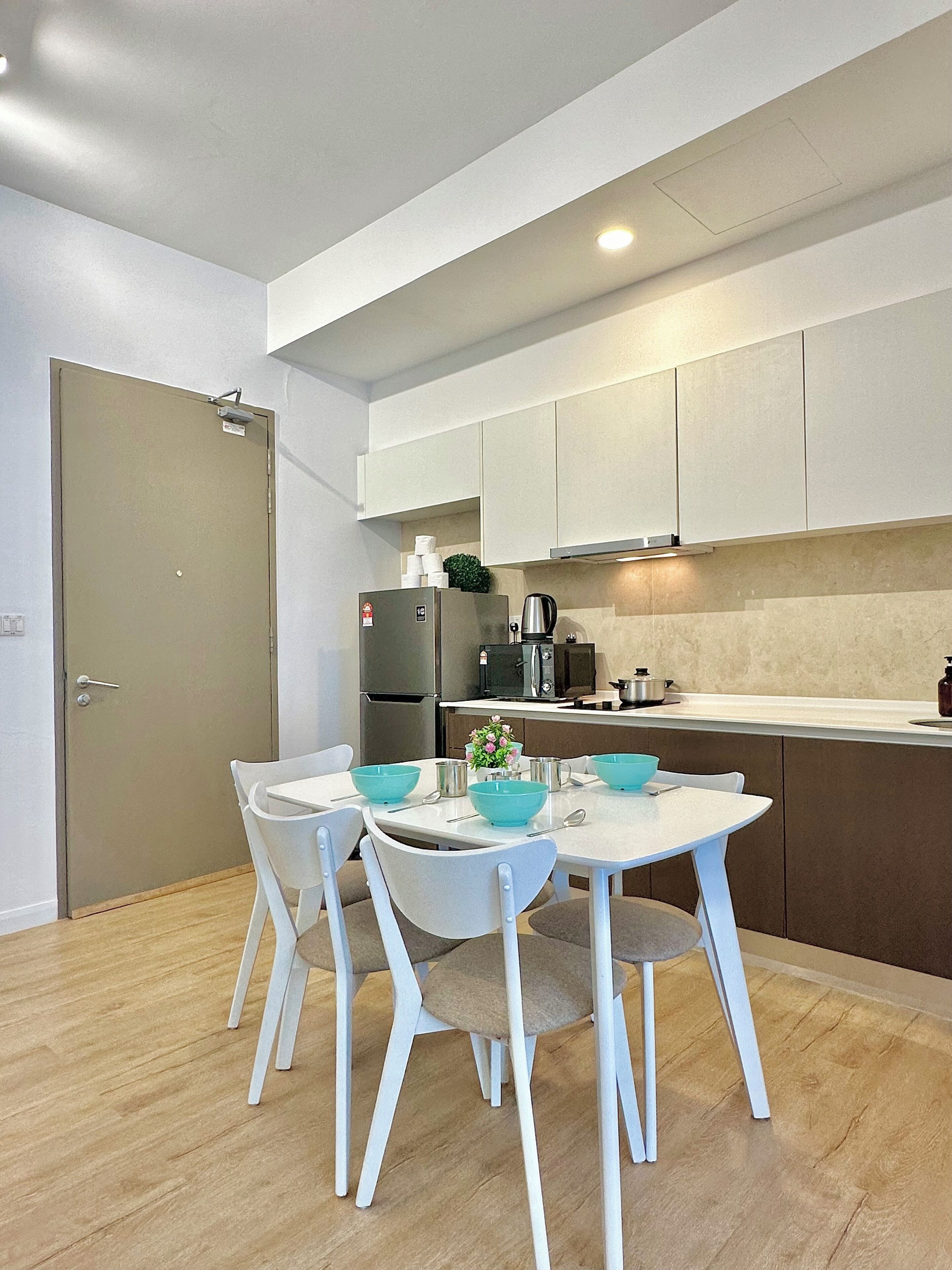 A modern kitchen with white cabinets, a built-in oven, and a microwave. There is a dining table with four chairs and blue bowls.