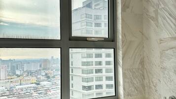 A bathroom with a bathtub, a window with a city view, and marble walls.