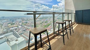 Un balcon avec vue sur la ville, deux tabourets et une rambarde en verre.