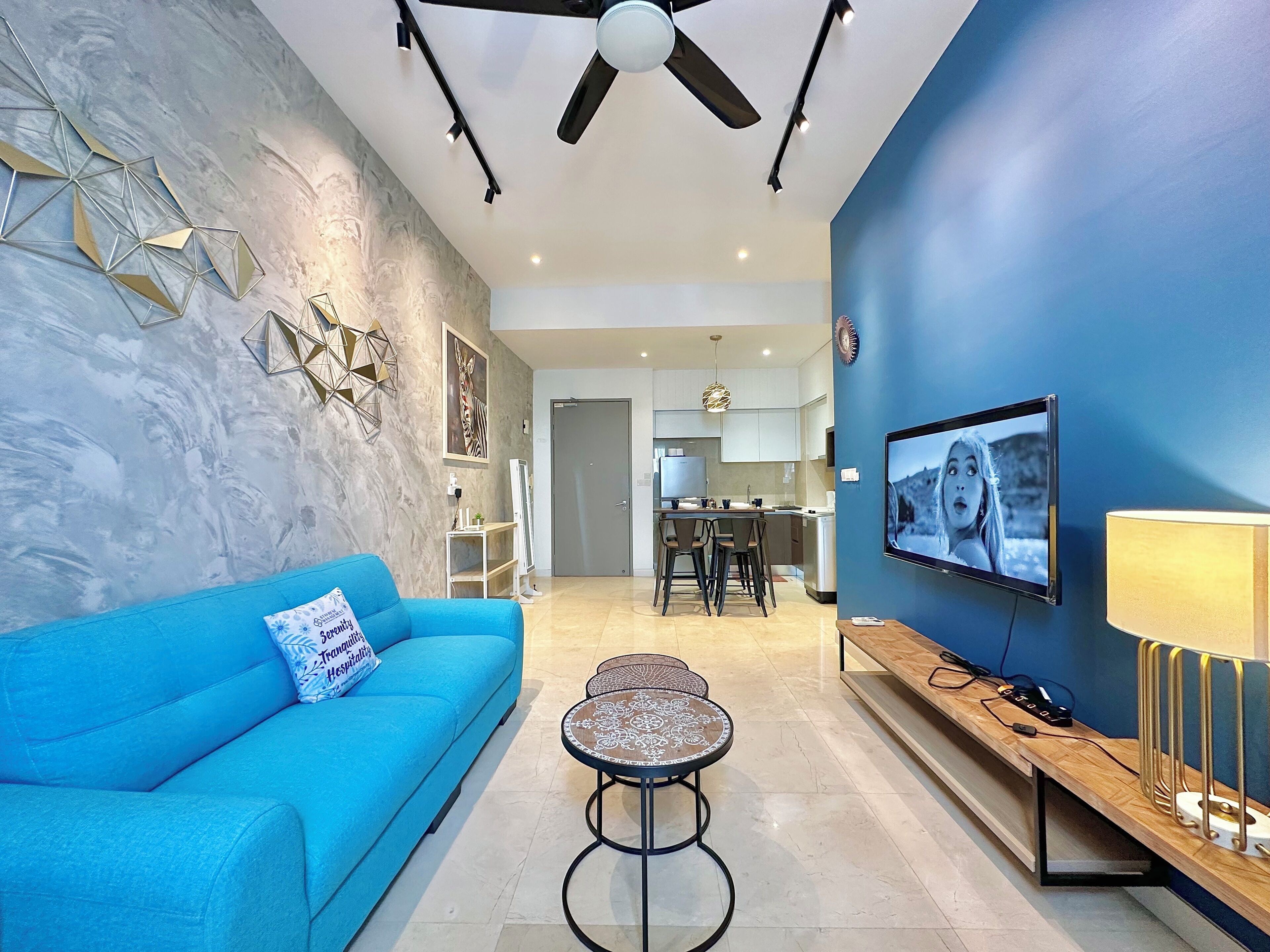 Una sala de estar moderna con un sofá azul, una mesa de centro, un televisor y un ventilador de techo.
