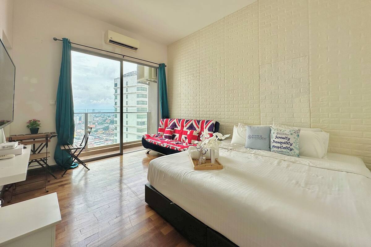 Habitación de hotel moderna con una cama grande, un escritorio y vistas a la ciudad a través de ventanales de piso a techo.