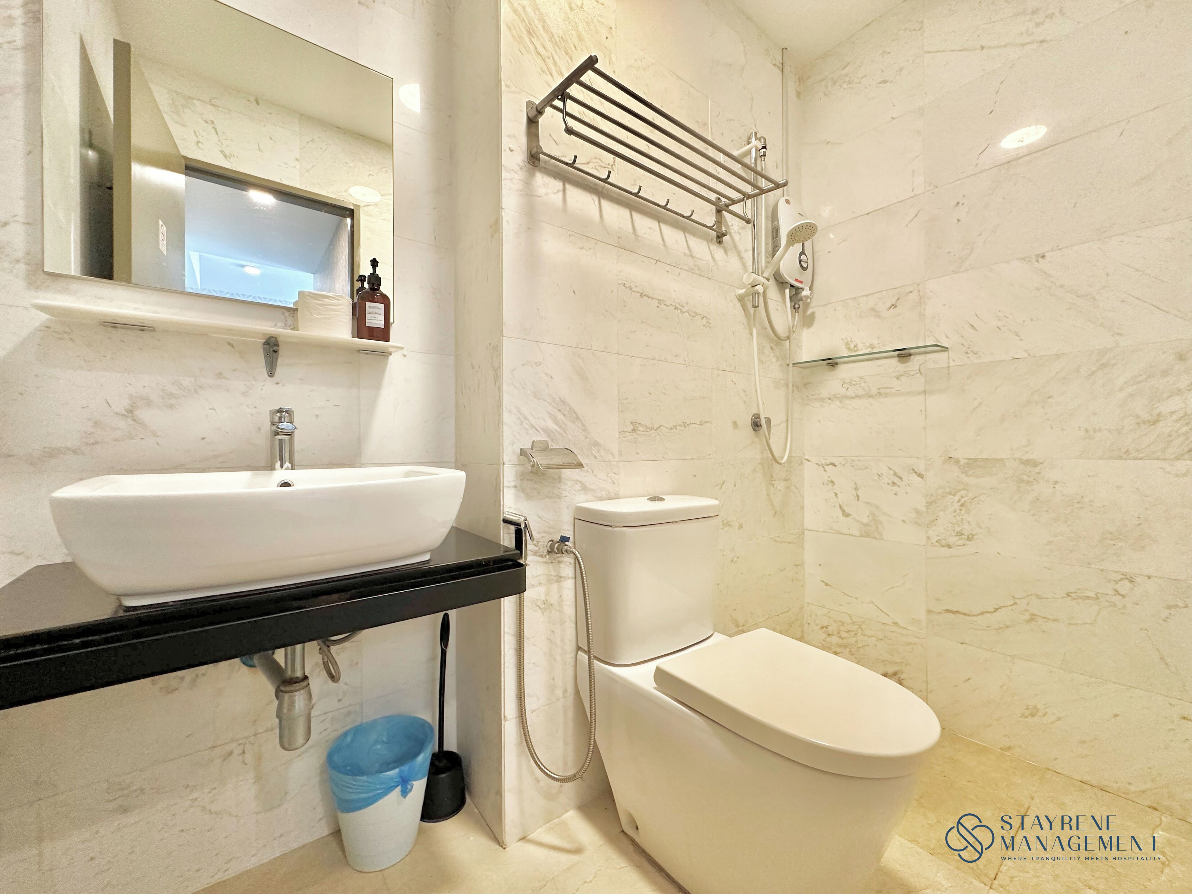 A bathroom with a white sink, black countertop, toilet, and a shower area with a towel rack.