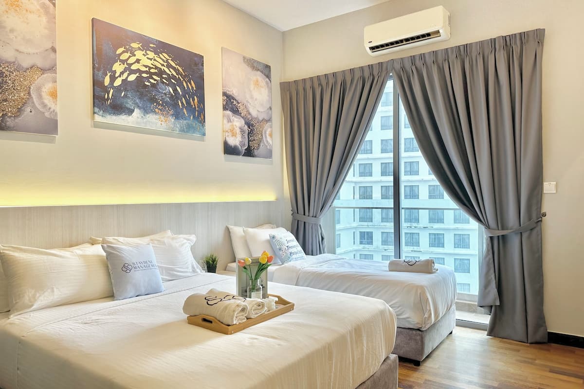 Habitación de hotel con dos camas, piso de madera y un ventanal con cortinas grises.