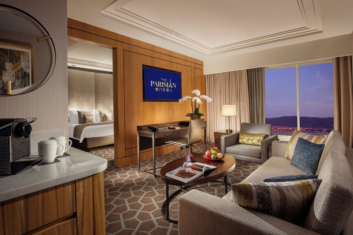 A hotel room with a bed, a desk, a sofa, a coffee machine, and a view of the city.