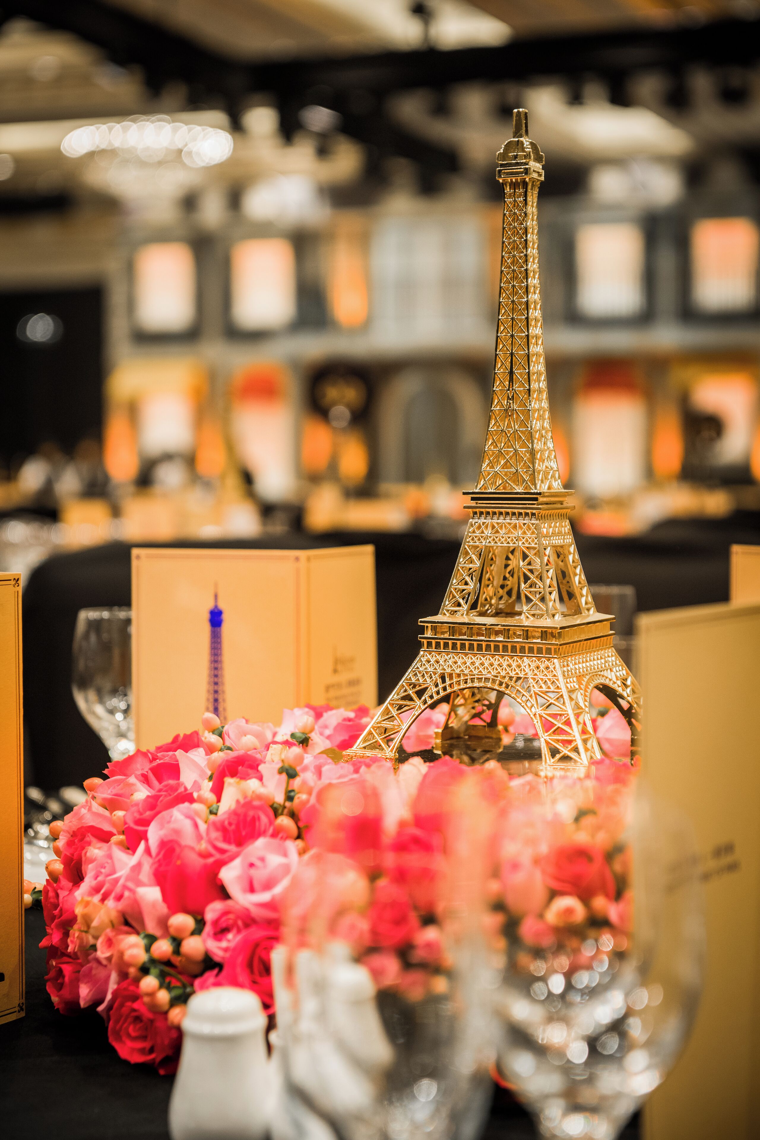 A table with a decorative Eiffel Tower centerpiece, surrounded by pink flowers and clear glassware.