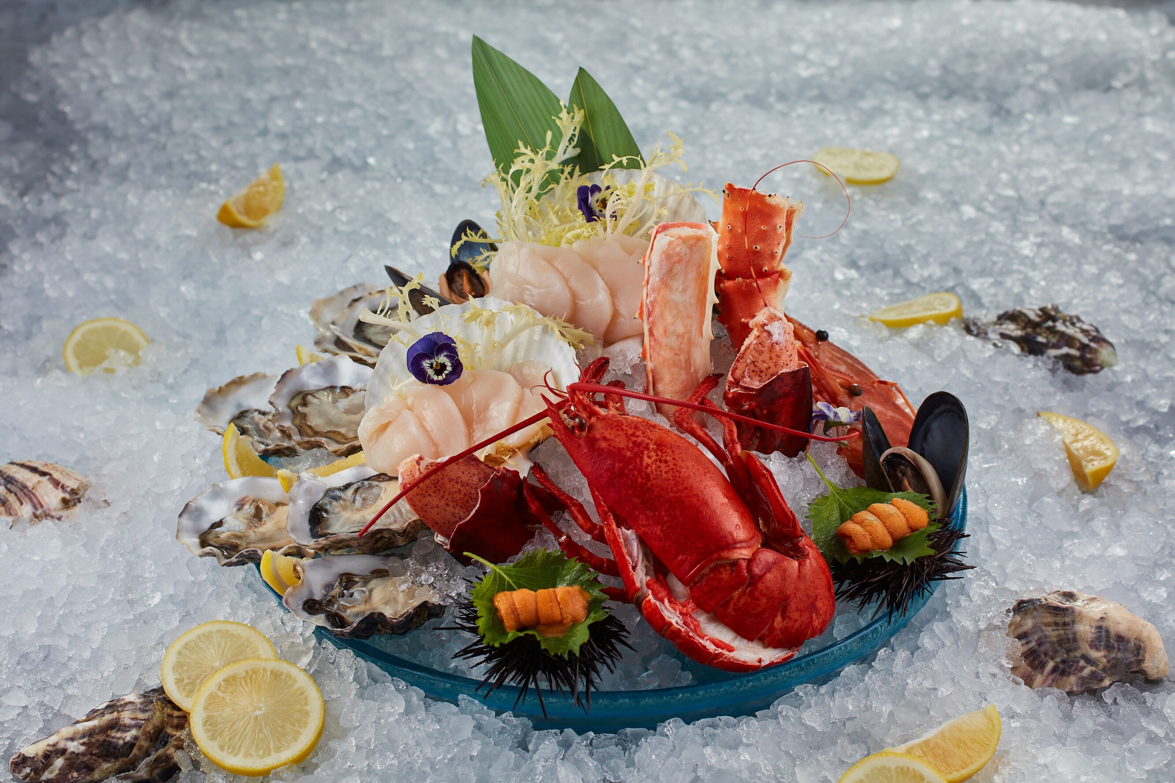 A seafood platter with lobster, mussels, oysters, and lemon slices on ice.