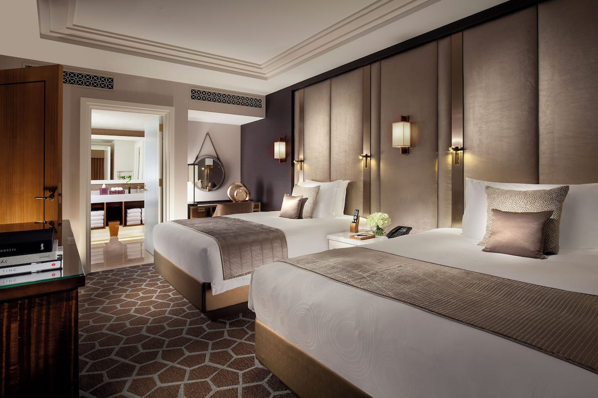 A hotel room with two beds, a wooden desk, a mirror, and a nightstand with a lamp.