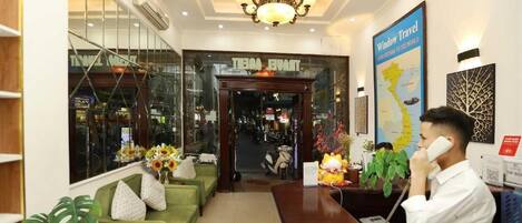 A hotel reception area with a reception desk, a chandelier, a map on the wall, and a sofa with decorative pillows.