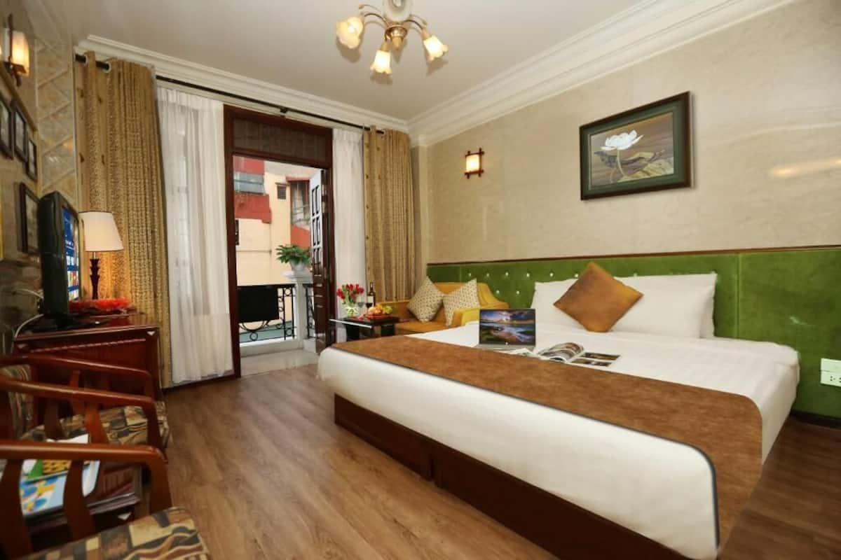 A hotel room with a bed, a desk with a lamp, a chair, a picture on the wall, and a view of the outside.