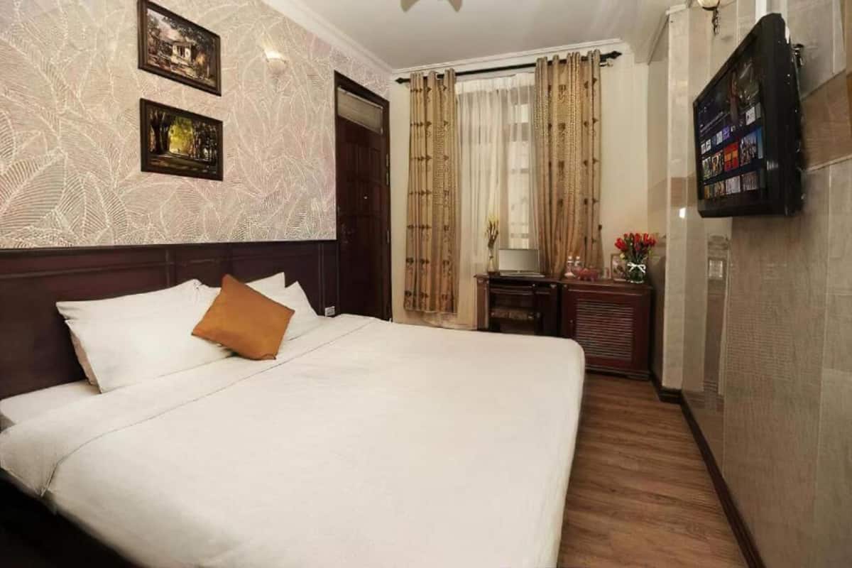 A hotel room with a large bed, a flat-screen TV mounted on the wall, and a wooden floor.
