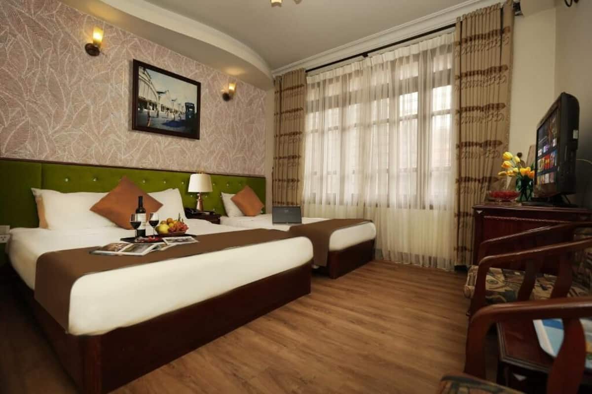 A hotel room with two beds, a desk with a laptop, a television, and a window with curtains.