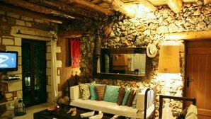 Ein gemütliches Wohnzimmer mit Steinwand, einem weißen Sofa mit gemusterten Kissen, einem Holztisch und einem Fernseher auf der linken Seite.