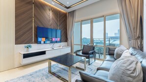 A modern living room with a flat-screen TV, a sofa, a coffee table, and a large window offering a city view.