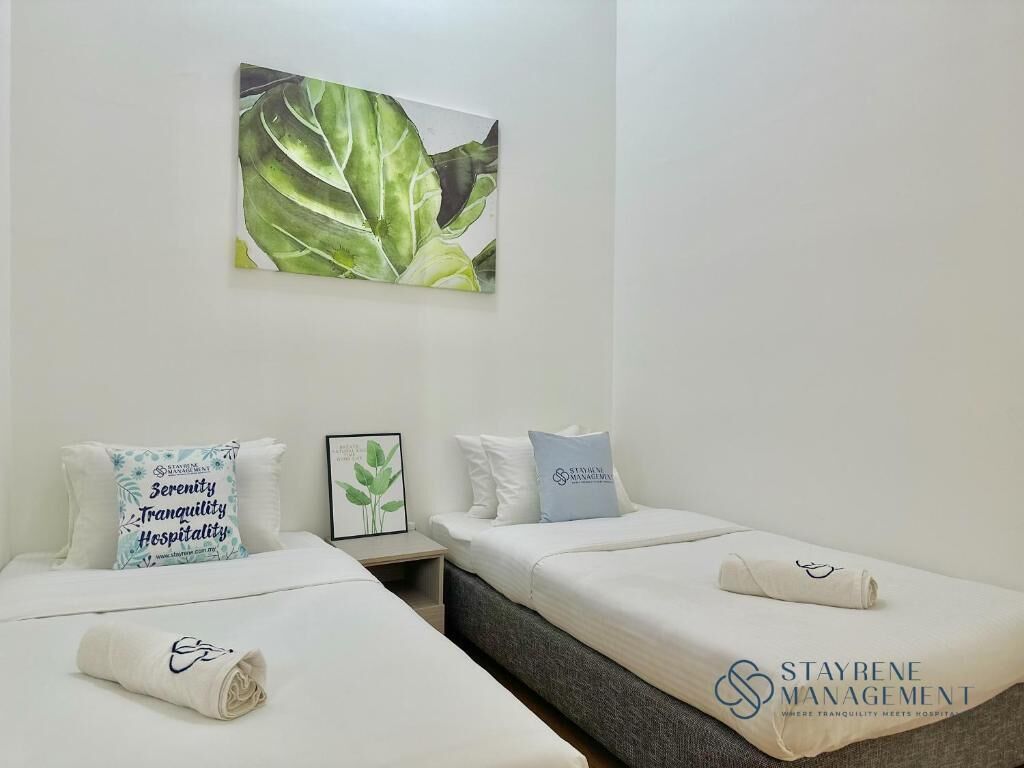 Ett hotellrum med två sängar, där varje säng har en prydligt vikt handduk och en kudde med hotellets logotyp. En inramad bild av löv hänger på väggen ovanför sängarna.