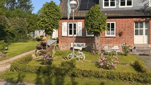 Ett hus med en fasad av tegel, solpaneler, en cykel och en trädgård med rosa blommor.