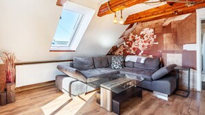 Ett modernt vardagsrum i loftstil med ett sluttande tak, ett soffbord i glas, en grå soffa och ett trägolv.
