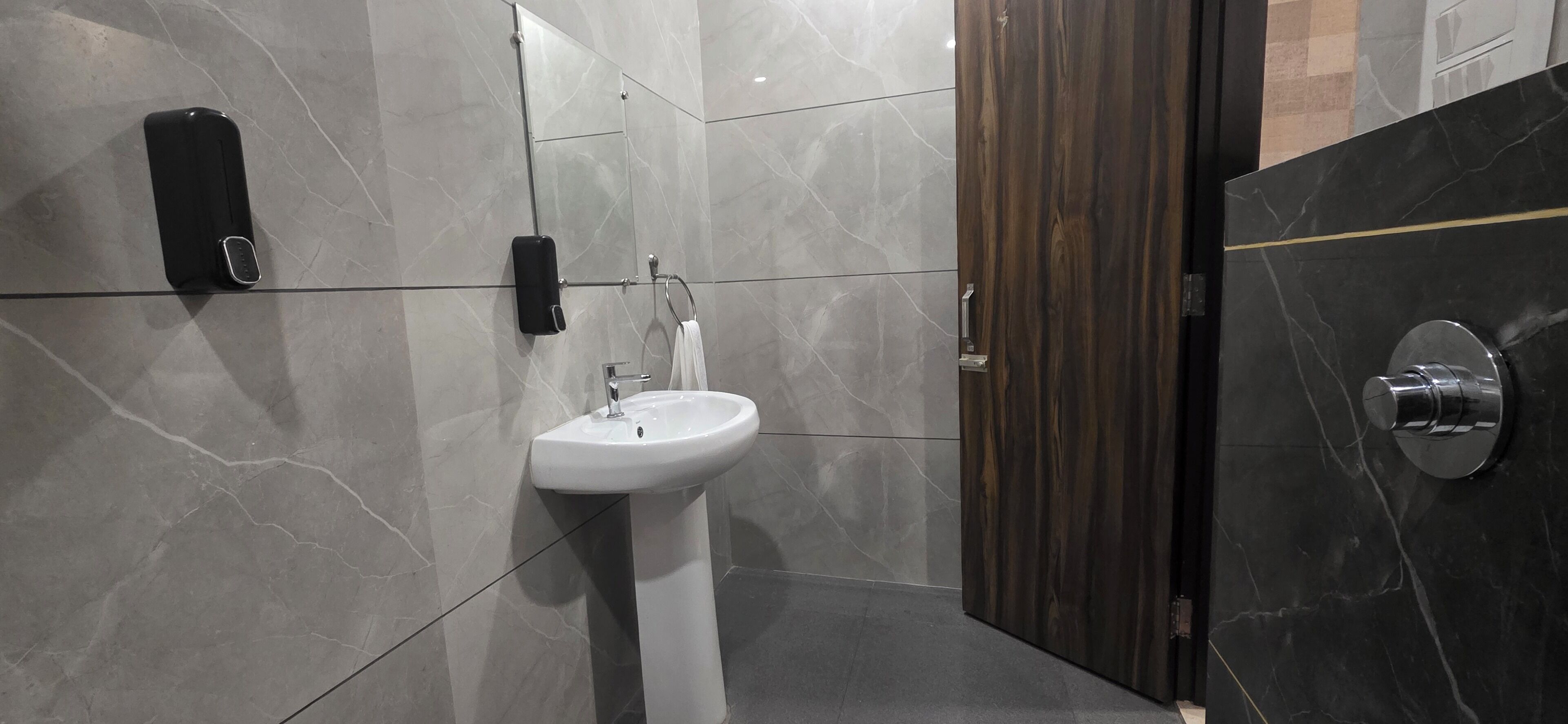 Un baño moderno con un lavamanos pedestal blanco, un dispensador de jabón de mano y un perchero para toallas.