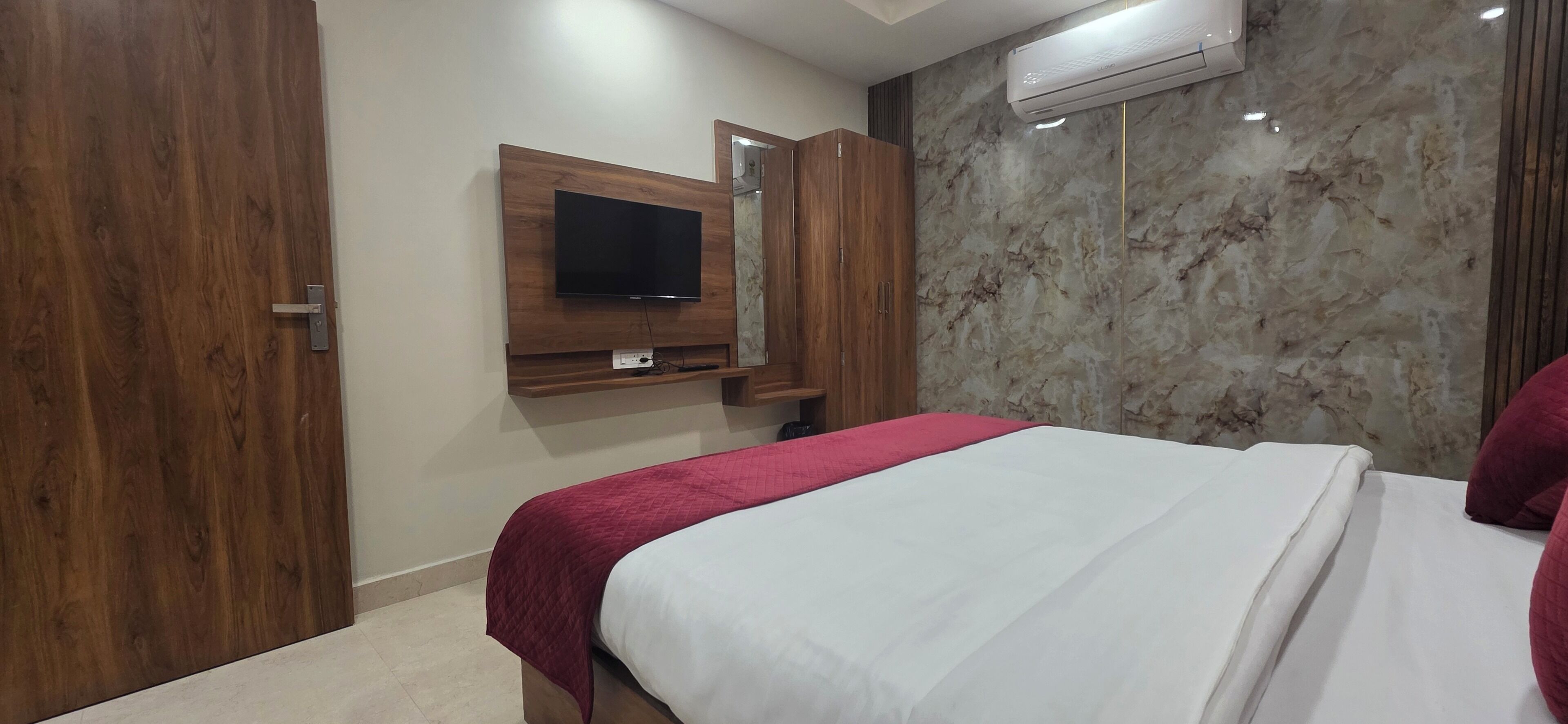 Habitación de hotel con cama, televisor montado en un panel de madera, pared con diseño de mármol y unidad de aire acondicionado.