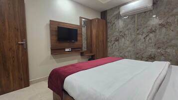 Habitación de hotel con cama, televisor montado en un panel de madera, pared con diseño de mármol y unidad de aire acondicionado.