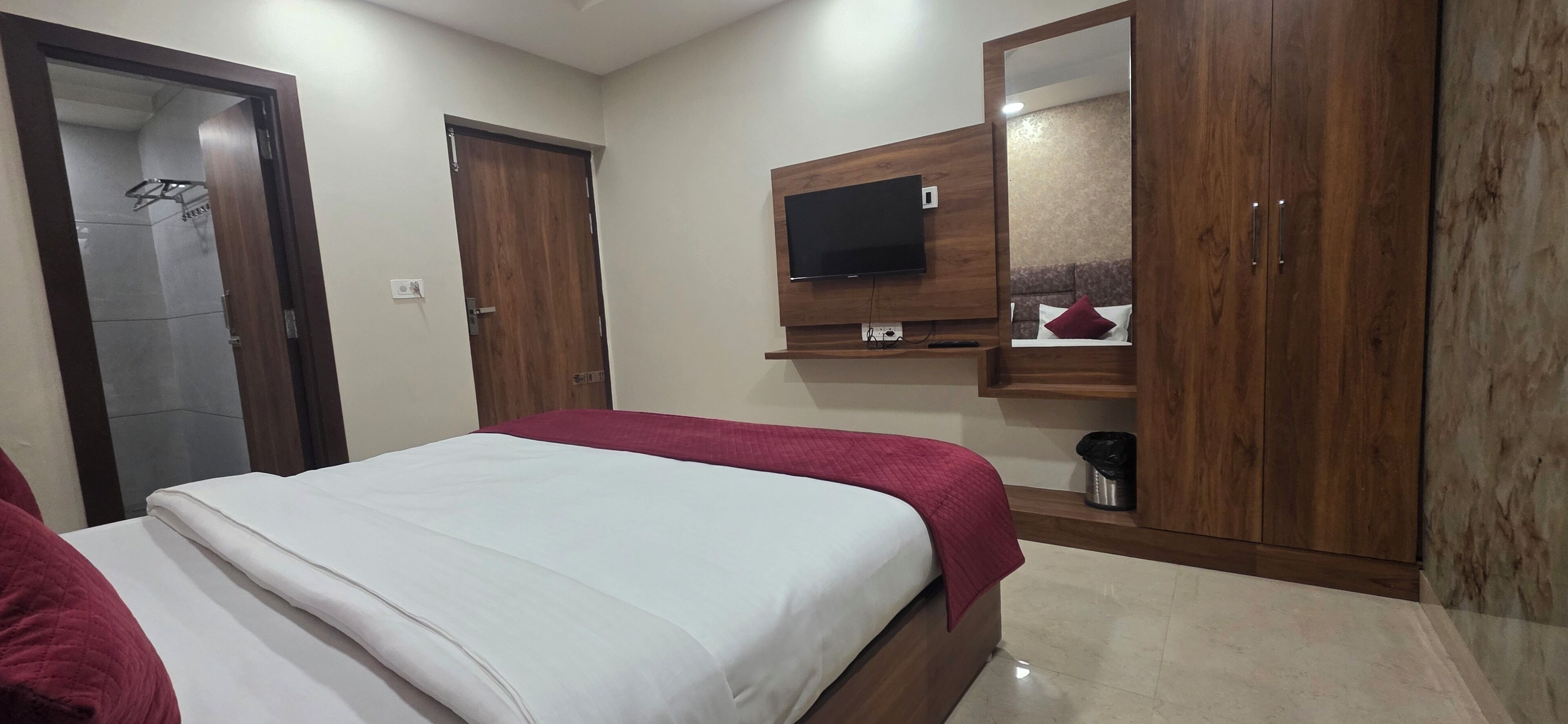 A bedroom with a bed, wooden wardrobe, a mounted TV, and a mirror.