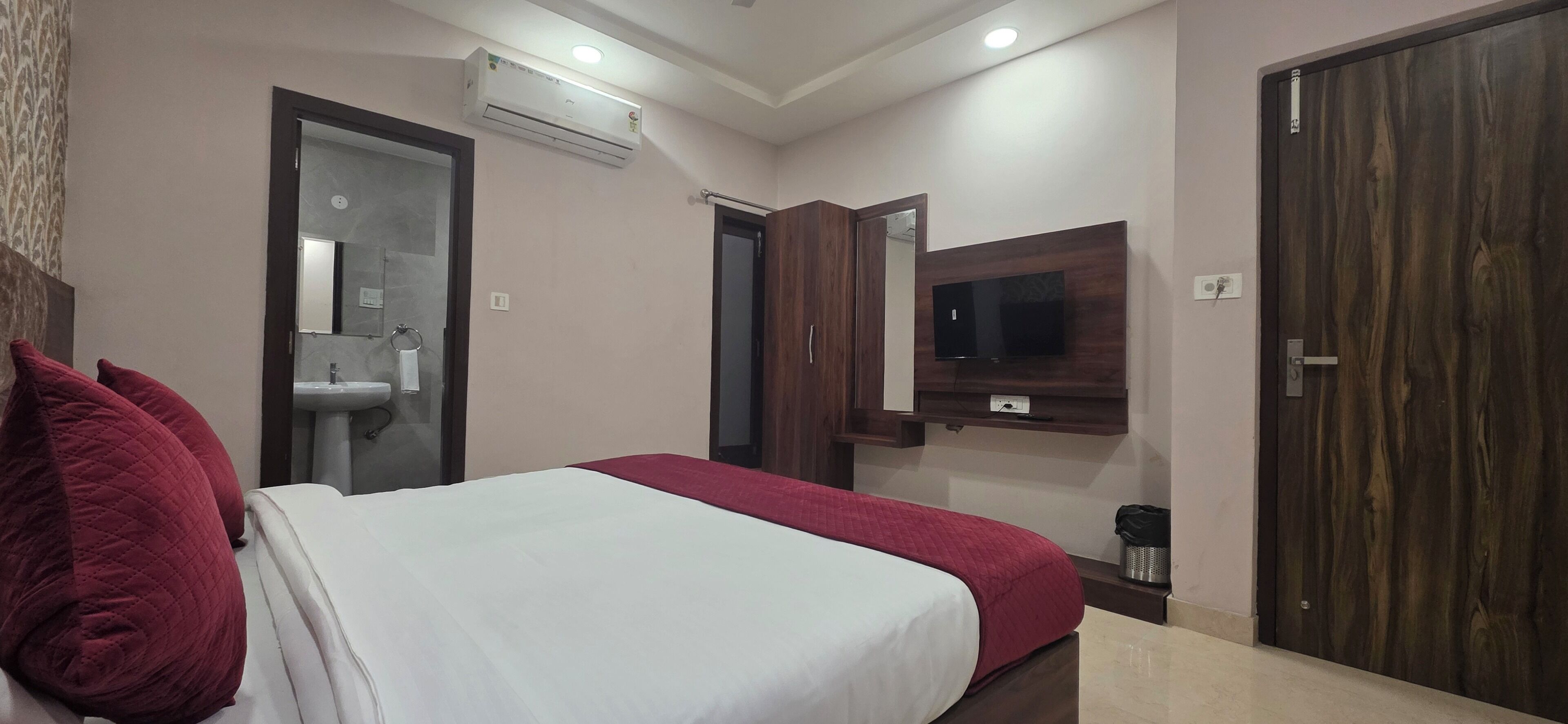 Una habitación de hotel con cama, espejo, armario, televisor y aire acondicionado.