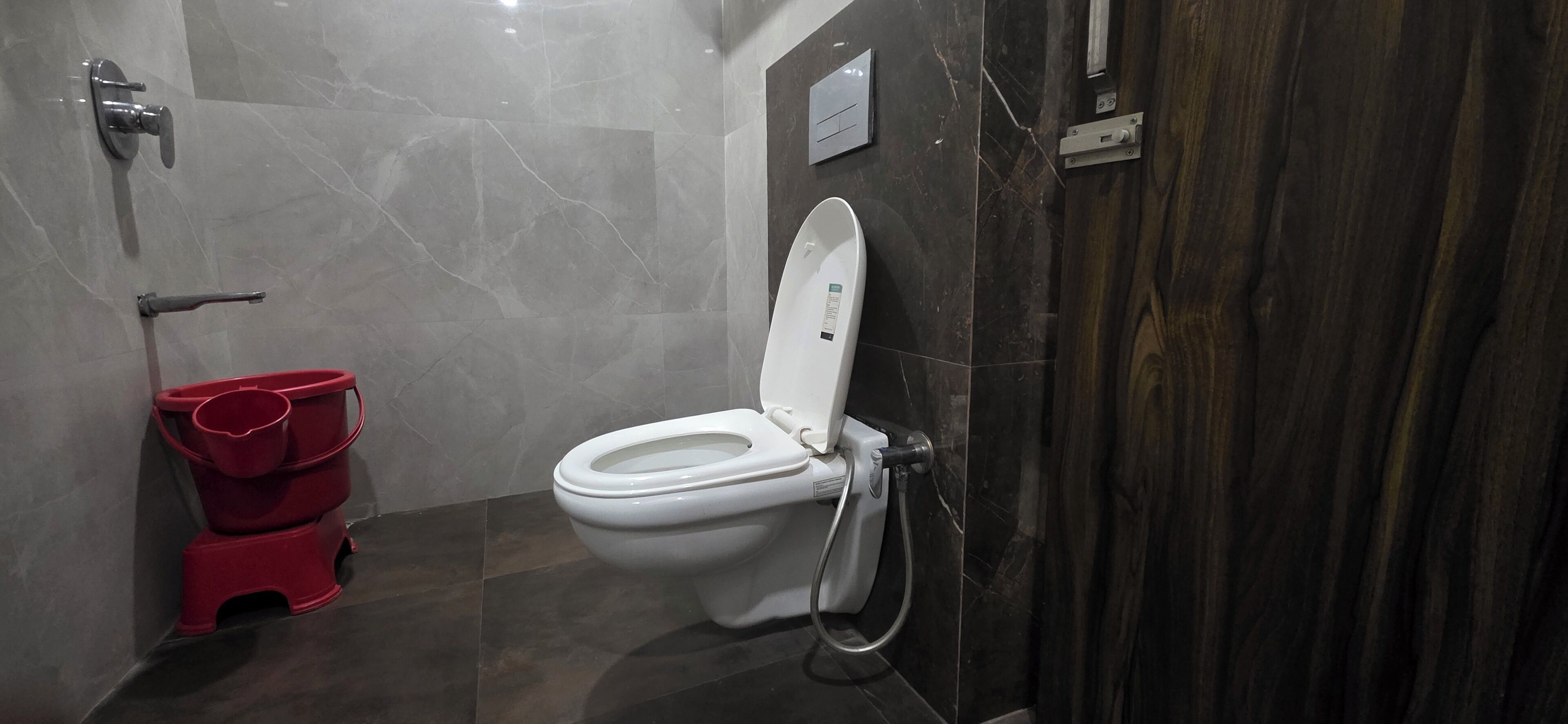 A modern bathroom with a white toilet, a red bucket, and a marble floor.