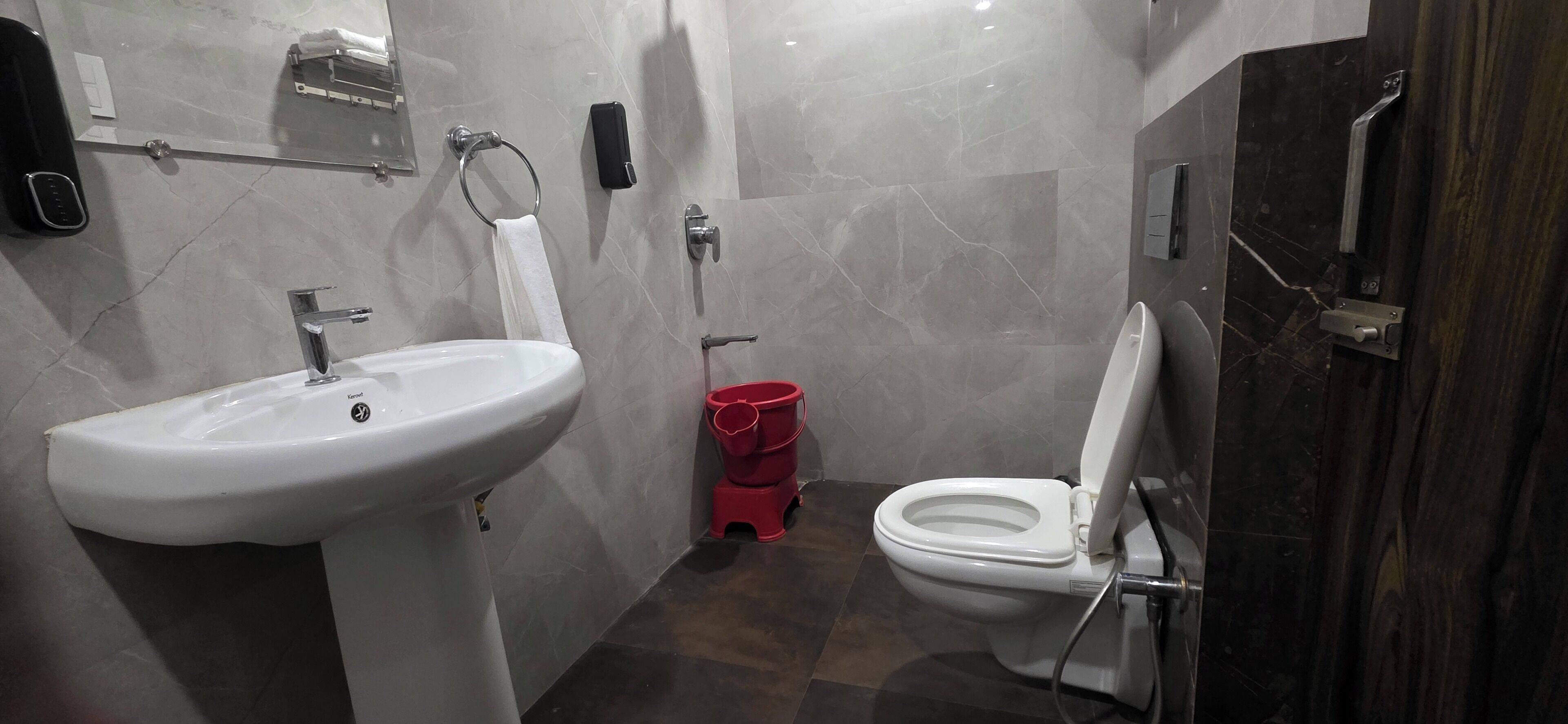 A bathroom with a white sink, a toilet, and a red trash bin.