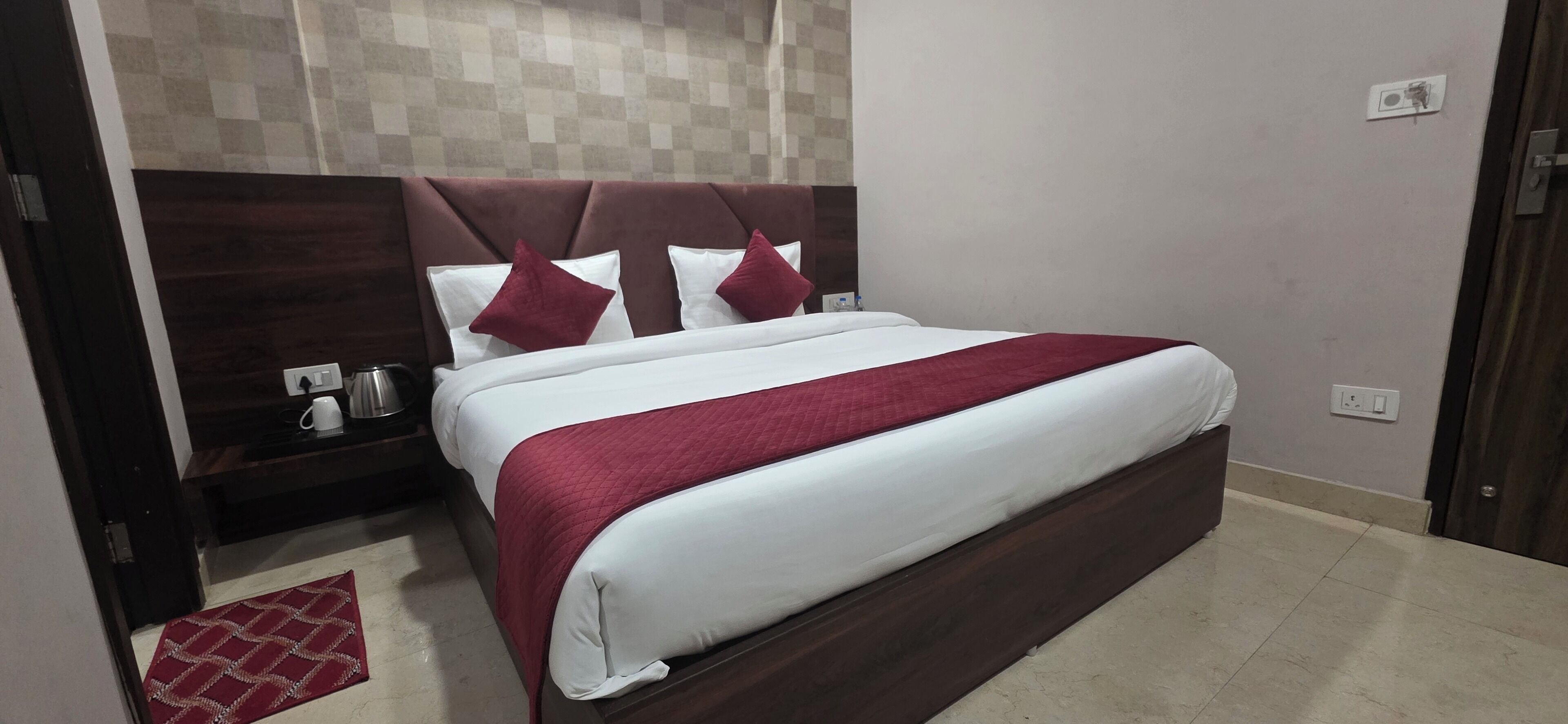 A neatly made bed with a red blanket, a wooden headboard, and a checkered wall behind it.