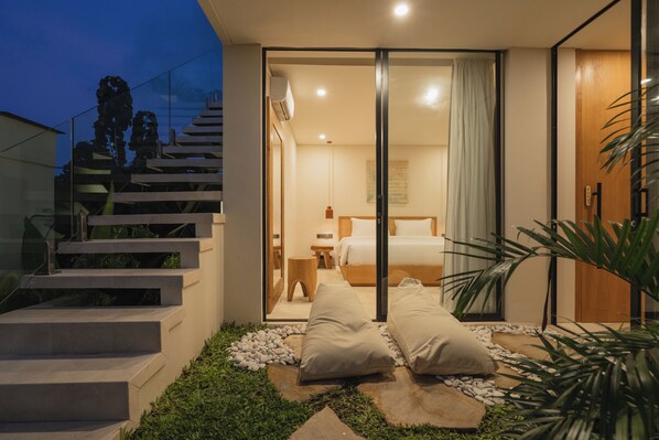 Une chambre à coucher moderne avec une porte en verre donnant sur une salle de bain, un escalier et un petit espace extérieur agrémenté de plantes.