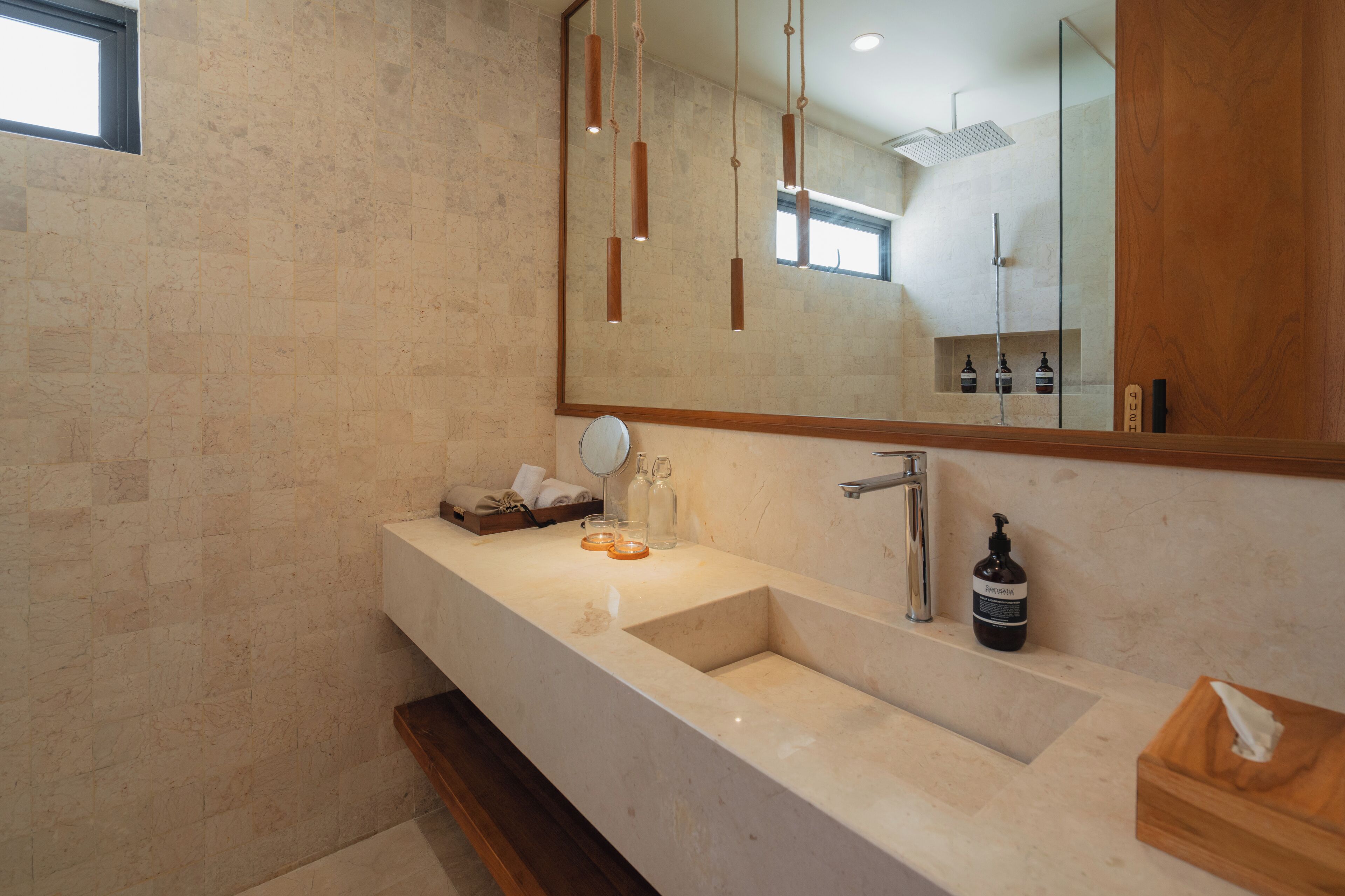 A bathroom with a large mirror, a sink, and hanging pendant lights.