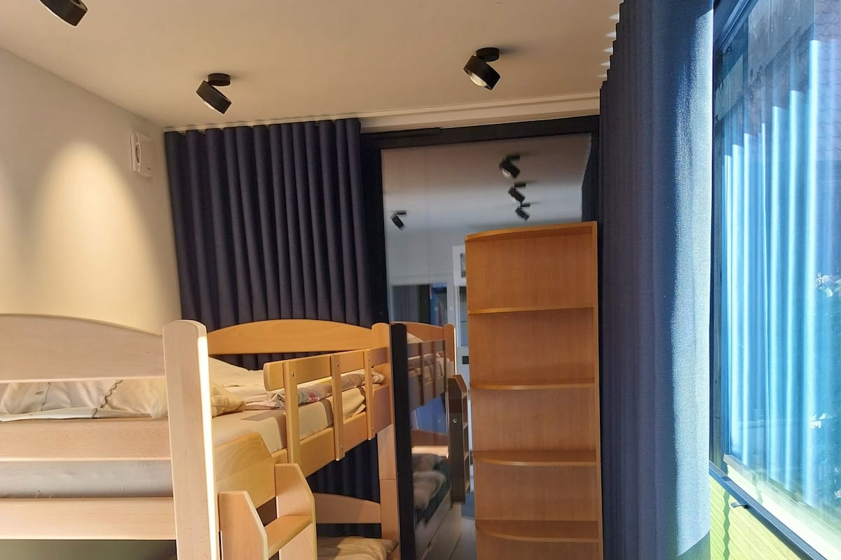 Habitación con literas, un escritorio de madera, una ventana con cortinas e iluminación empotrada en el techo.