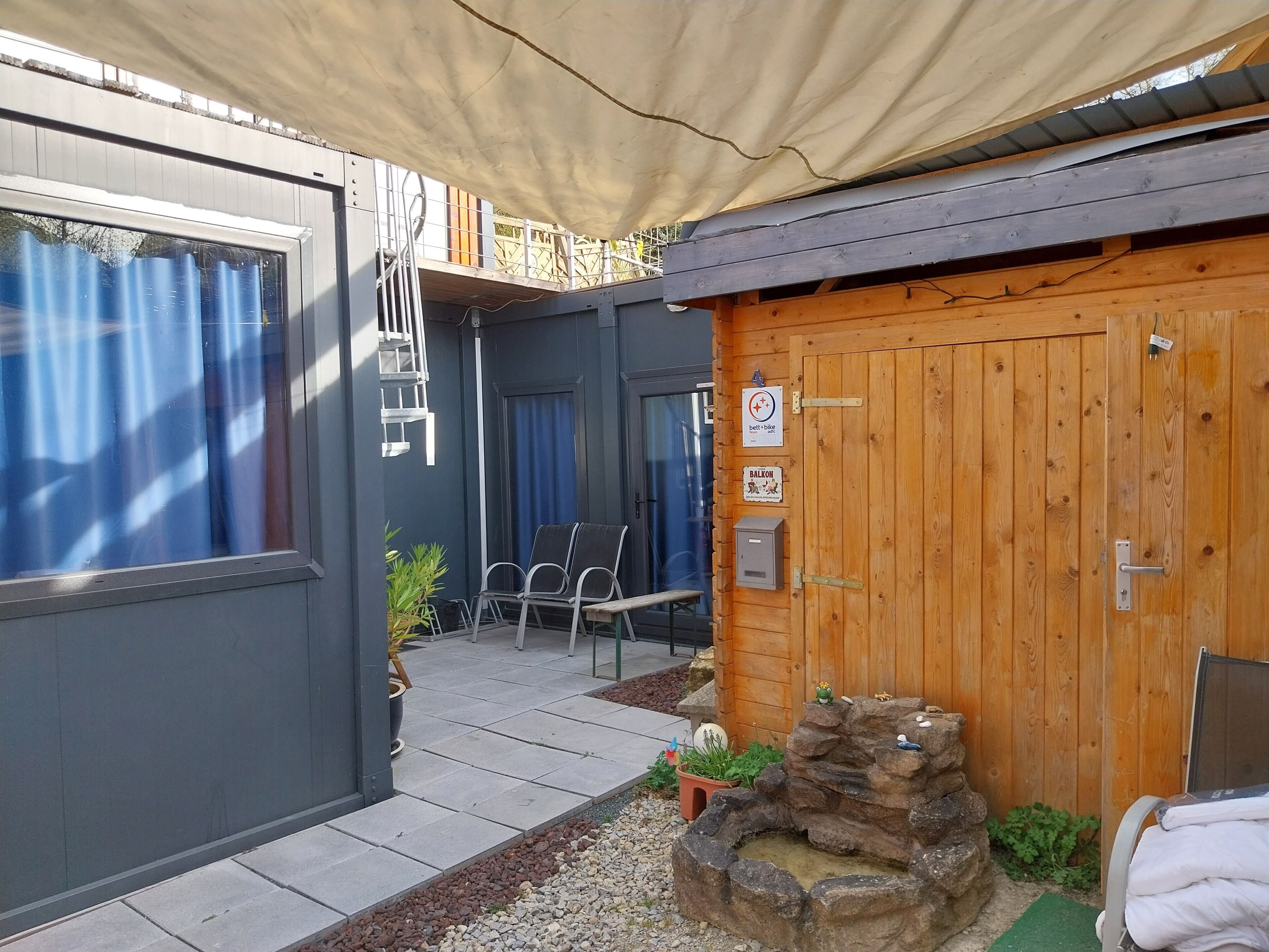 Una cabaña de madera con balcón, un pequeño estanque y una zona de estar cubierta.