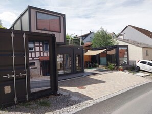 A modern building with a large glass window, a covered outdoor seating area, and a parked car. - Kreativhof BIOTOPIA RadApart  (Creglingen)