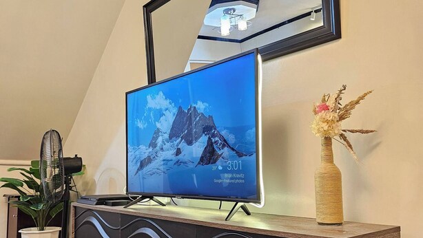 Moderni olohuone, jossa on litteänäyttöinen televisio puisen konsolipöydän päällä, suuri peili television yläpuolella ja ruukkukasvi television vieressä.