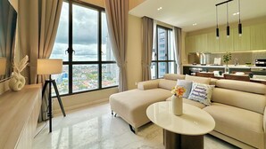 A modern living room with a sofa, a coffee table, and a view of the city through large windows. - Setia Sky 88 Johor Bahru by Stayrene (Johor Bahru)