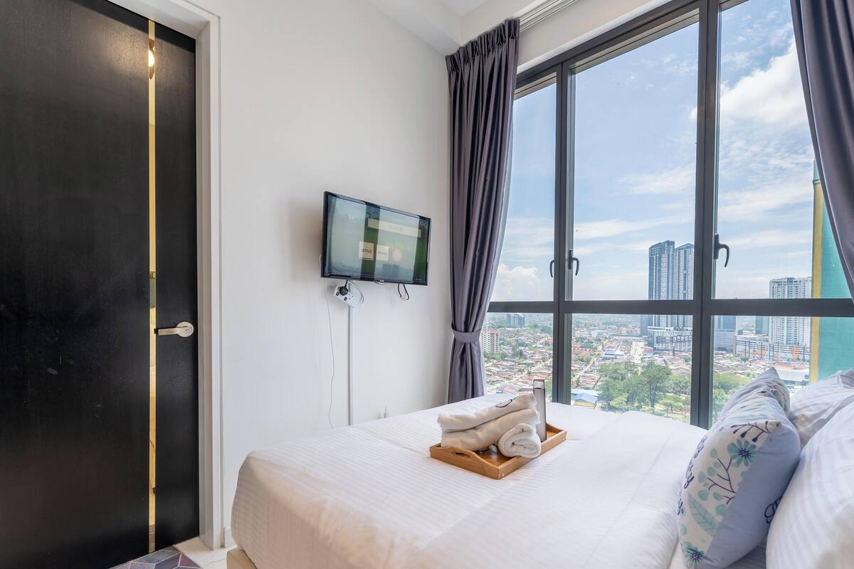 Una camera d'albergo con un letto, una televisione, una finestra con tende e vista sulla città.