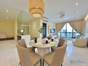 A modern living room with a round dining table, comfortable seating, a large window with a city view, and a ceiling fan. - Setia Sky 88 Johor Bahru by Stayrene (Johor Bahru)