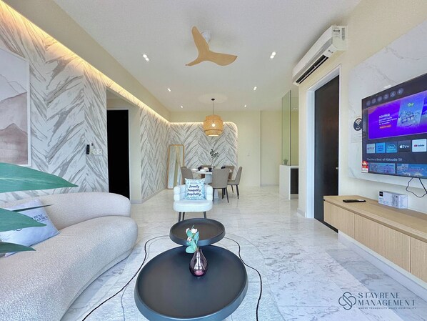 A modern living room with a sofa, a coffee table with a vase, a dining area with a table and chairs, and a TV mounted on the wall displaying various channels. - Setia Sky 88 Johor Bahru by Stayrene (Johor Bahru)