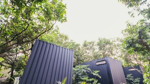 Two black modular cabins with red bases, surrounded by greenery. - MRUDA FARMSTAY (Dahanu)